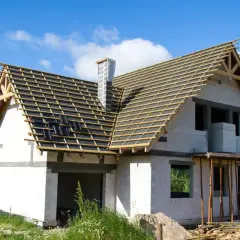 Budowa domu z białej cegły, z widoczną konstrukcją dachu i kominem.