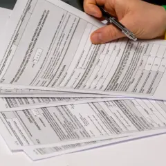 Dłoń z długopisem nad stosem dokumentów podatkowych PIT.