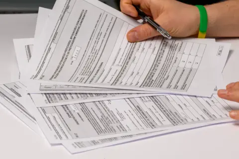 Dłoń z długopisem nad stosem dokumentów podatkowych PIT.